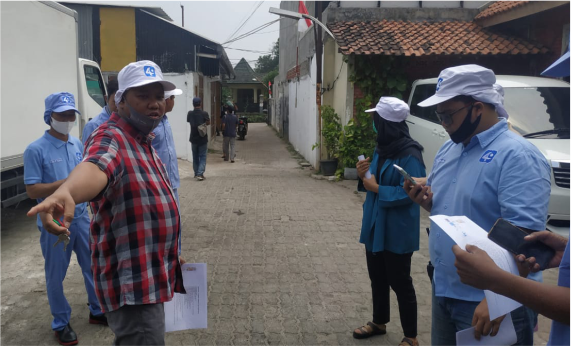 Sekelompok orang berdiskusi di jalan dengan kendaraan dan bangunan di latar belakang.